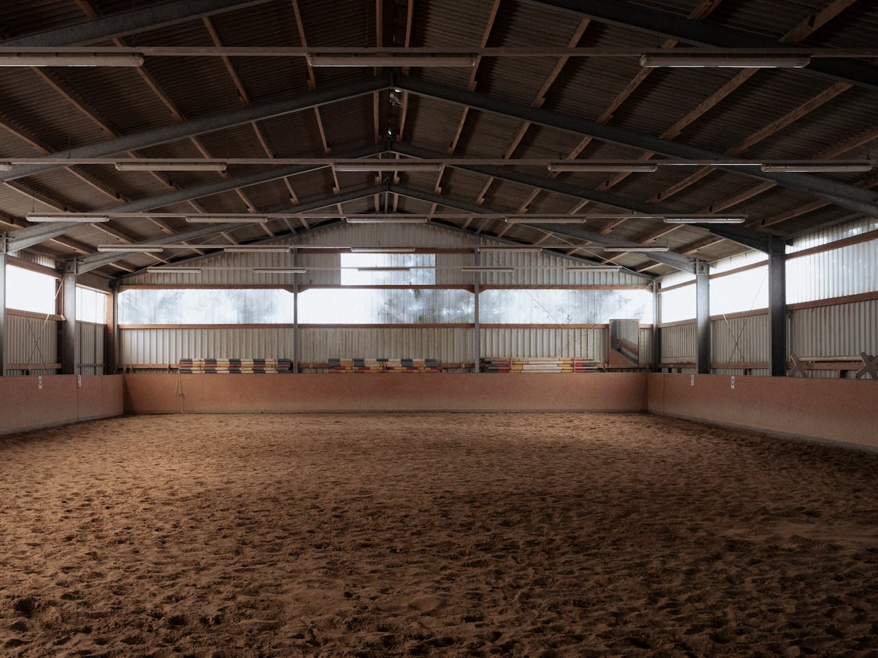 Wide view of an empty indoor riding arena with sandy floor and steel roofing, suitable for equestrian events.